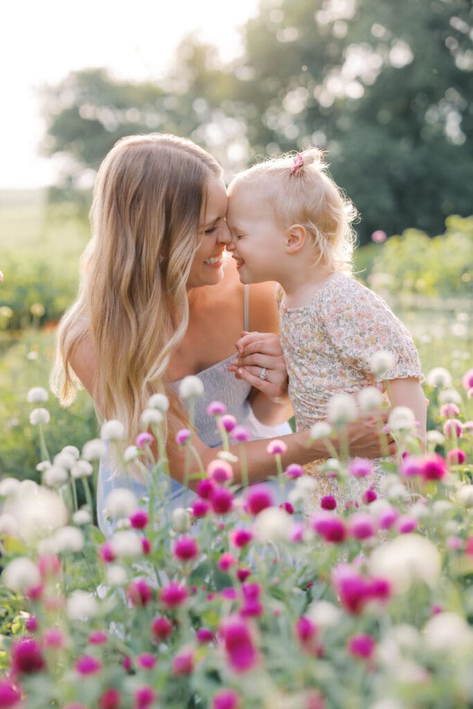 a mother holds her daughters hands as they laugh together in a field of flowers during their Minneapolis Family Photos