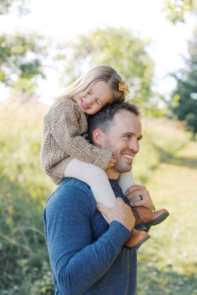 a girl sits on her dad's shoulders during their Lakeville Family Photos.